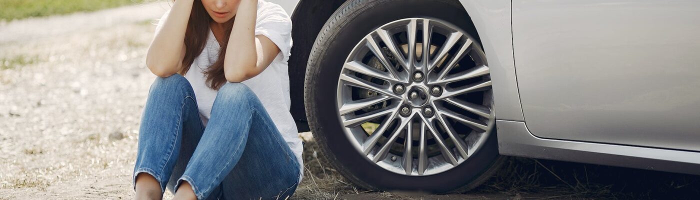 worried young woman sitting near broken automobile at roadside in countryside