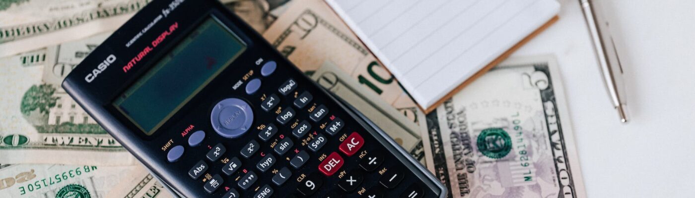 calculator and notepad placed on usa dollars stack